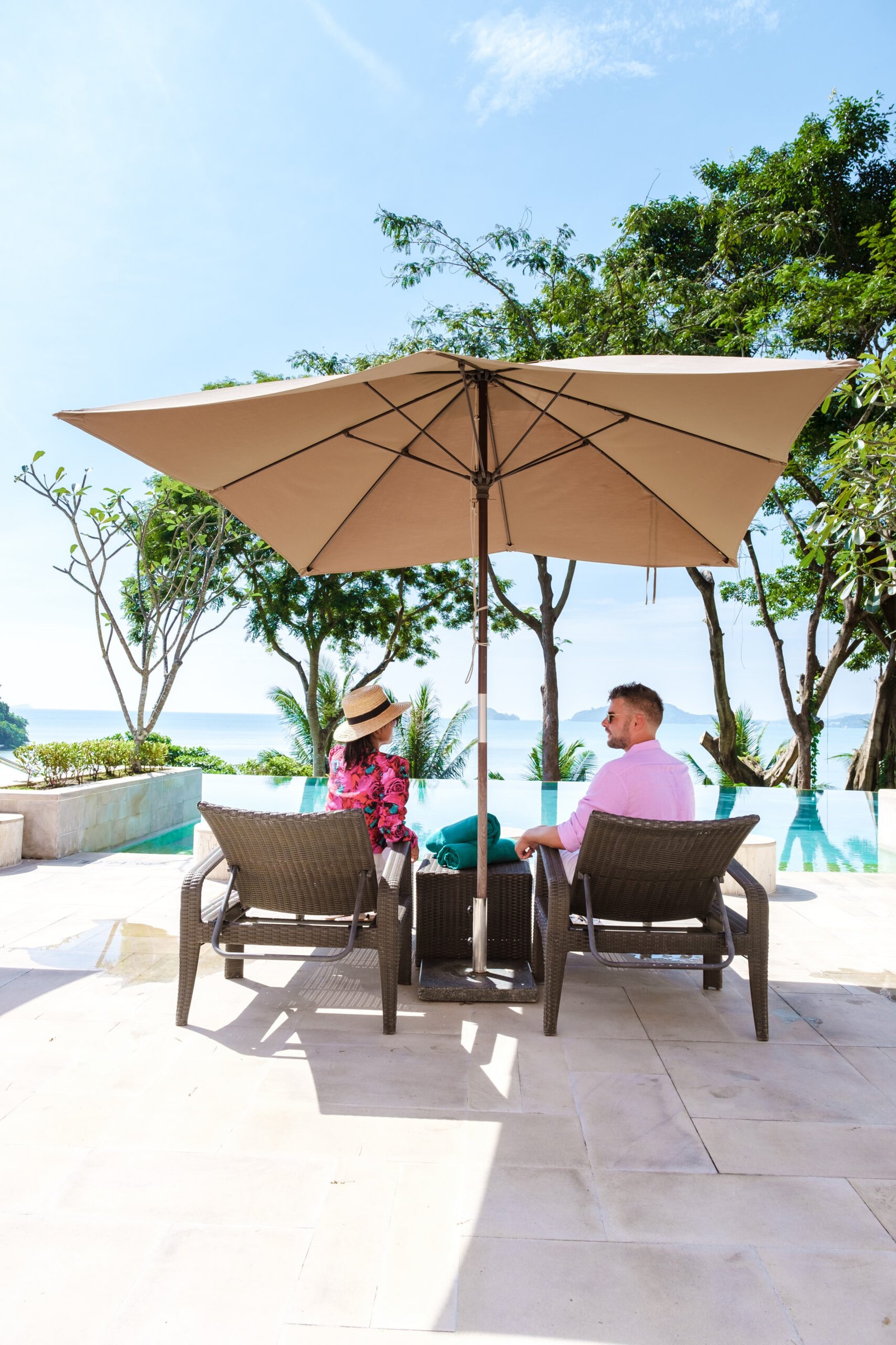 couple man and woman mid age at a luxury beach chair, on a luxury vacation in Thailand, men and an Asian woman in a pool looking out over the bay watching the sunset. Infinity pool over the ocean